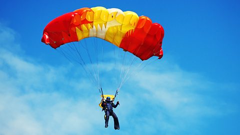 A person in the air with their parachute open after having jumped 