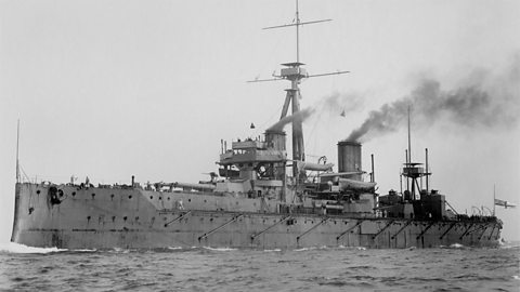 A dreadnought battleship in the sea, with plumes of smoke coming out of its chimneys. 