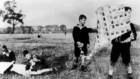 Four children in a field. Two are holding up a kite made from banknotes. 