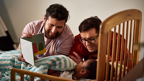 Two dads read a story to their daughter in bed.