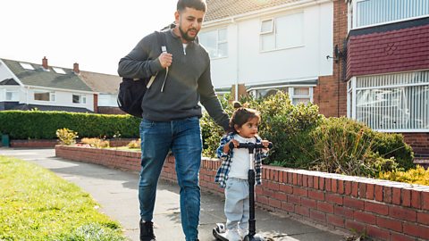 Dad walks to school with his young child on a scooter.