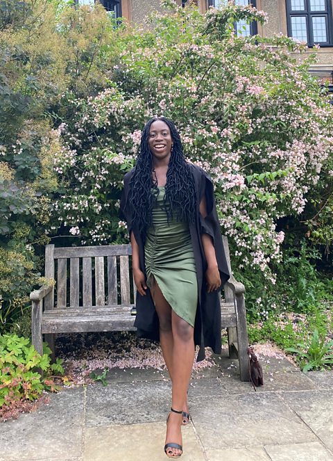 Tolu wearing a green dress in front of a bench and some greenery