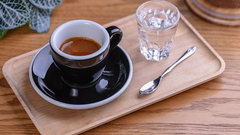 A cup of tea with a matching saucer and glass of water, sitting on a wooden tray 