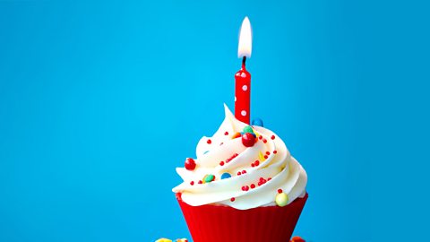 A decorated cupcake with red casing and a lit single red candle on top