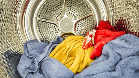 A stack of multi-coloured items, including towels and other clothing, inside a tumble dryer. 