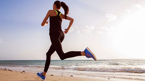 A woman, dressed in athletic clothing, running along the beach