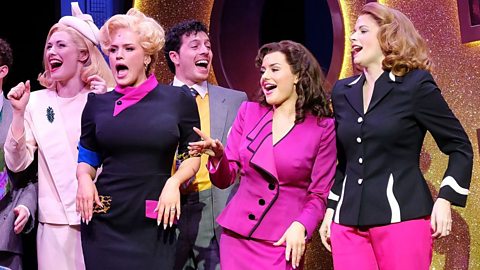 Four actresses in brightly coloured power suits, sing on stage at a performance of 9 to 5: The Musical.