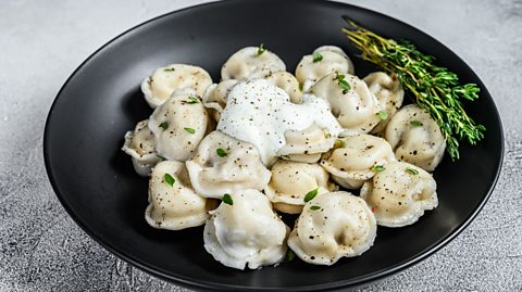 Pelmeni in a bowl with herbs and sour cream