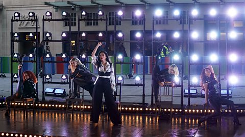 The Pussycat Dolls during a live performance doing some high kicking dance moves.