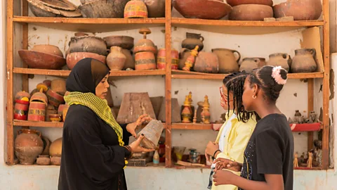 Mai Farouk Amberkab uses a traditional copper weight to explain the traditional barter economy to Tarek and Merghany (Credit: Mai Farouk)