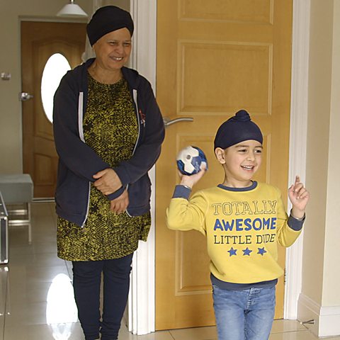 A young boy is throwing a ball while his grandma smiles behind him