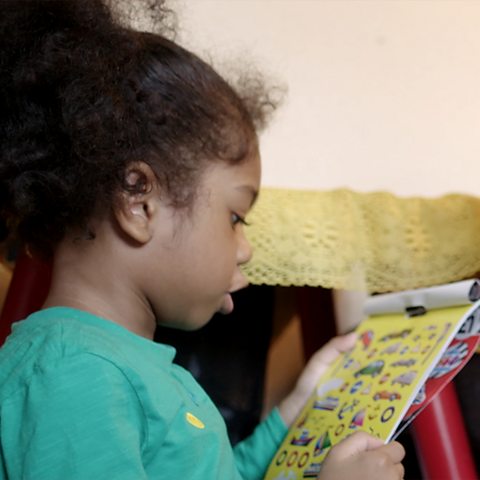 A young girl is looking at a pad of stickers and talking about them.