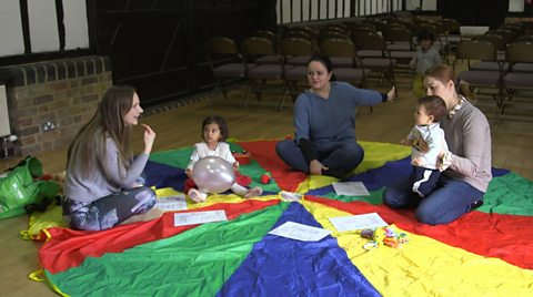 Three children at a playgroup siting on the floor doing an activity with three adults. 