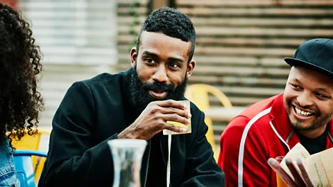 Getty Images Two people holding mugs converse on a bench outside a coffee shop