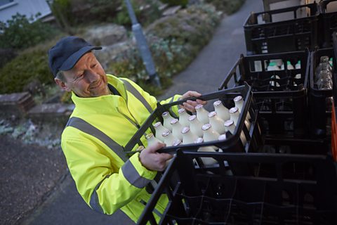 Milkman lifting a crate of milk of his float