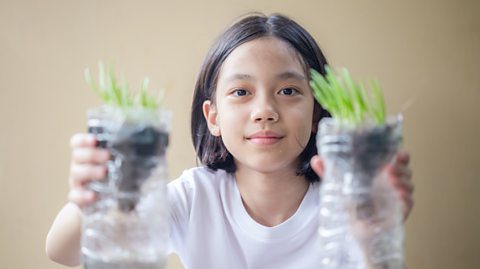 A child with two plants growing inside recycled plastic bottles