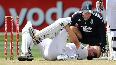 a cricket player lying on the ground holding his knee