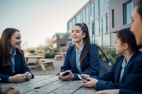 Teenagers chatting outside of a school on a wooden table.