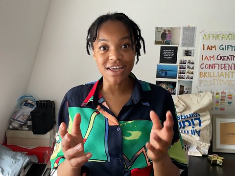 A young person talks animatedly to the camera in her bedroom.