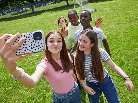 A group of teenagers take a selfie together outside in a sunny park