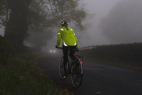 Woman in reflective coat cycling in fog