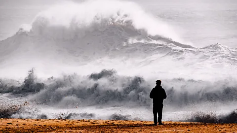 Rytis Seskaitis/Getty Images Man looking out to huge waves in Nazaré, Portugal