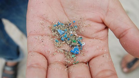 tiny bits of plastic and sand in a person's hand