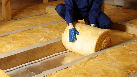 Construction worker rolling out thermal insulation in an attic.