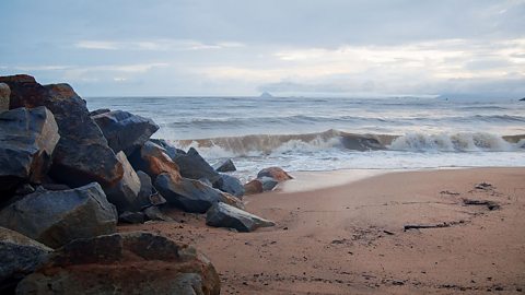 Large black rocks sittting on a beach near the sea front. 