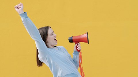 Portrait of woman yelling at megaphone and pronouncing a speech while raising an arm.