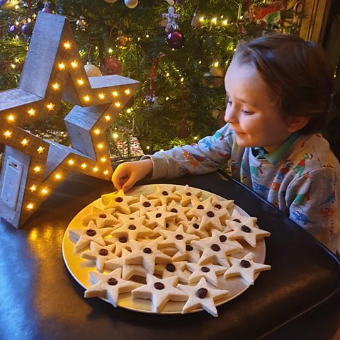 A child sitting at a table with a Christmas tree, a light up star and lots of shortbread stars.