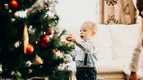 A young boy in a nice shirt is adding a bauble to his christmas tree.