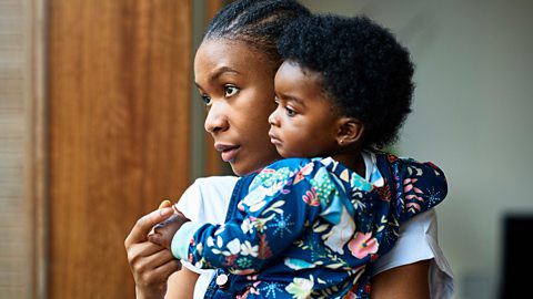 A mum hold her baby and looks out the window mournfully.