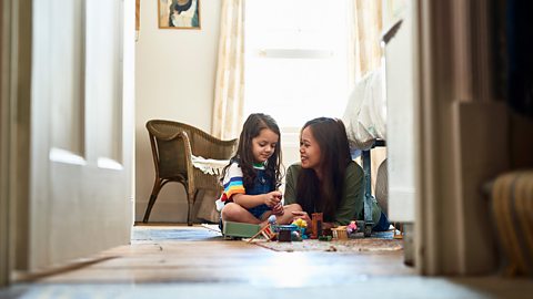 A mother and her daughter are playing games on the floor of a bedroom.