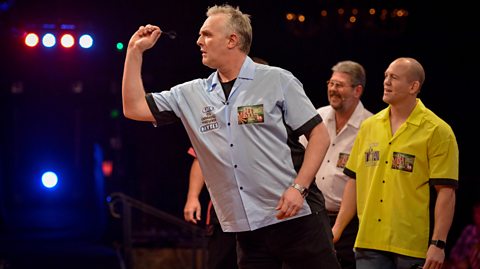 Greg Davies throws a dart while Mike Tindall watches on as part of the 2016 television programme Let's Play Darts for Sports Relief.