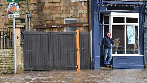 Man standing on a shop step as the road and footpath around him is covered in flood water