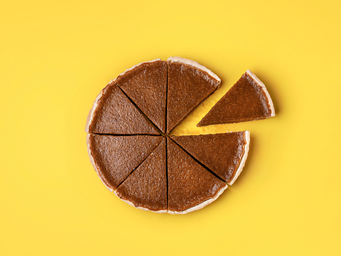 A pumpkin pie divided into eight equal slices. It is isolated and set on a yellow background. 