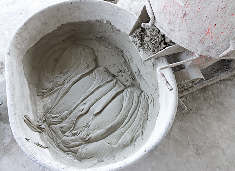 Cement in a bucket on a concrete floor. To the right, a material is about to be mixed in from a pourer.