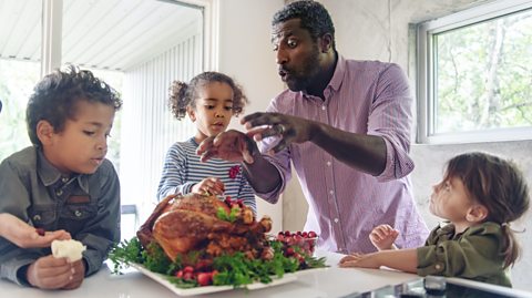 family at the kitchen table all looking at the turkey that their dad has presented to them