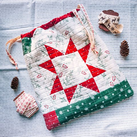 A patchwork giftbag surrounded by pine corns and ribbon.