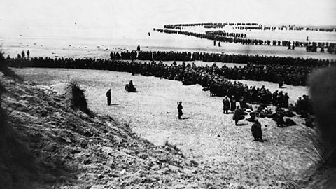 A black and white photograph of British and French troops waiting to be evacuated on the beaches at Dunkirk.