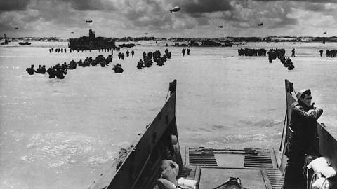 A black and white photograph showing US soldiers arriving on the beaches at Normandy on D-Day, 1944.