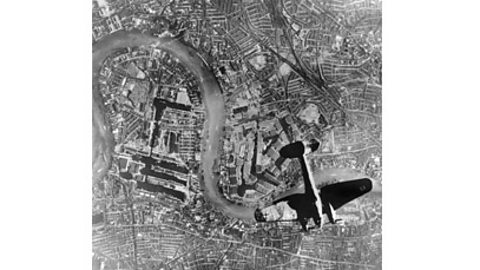 A black and white photograph of a German Heinkel bomber plane flying over London.