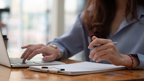 A photograph of a lady sitting at a table and using a laptop.