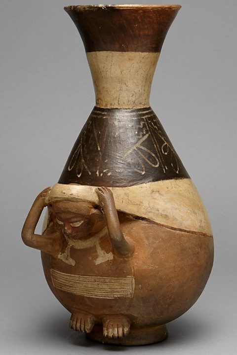 Bottle in the shape of a person carrying a load using a tumpline.