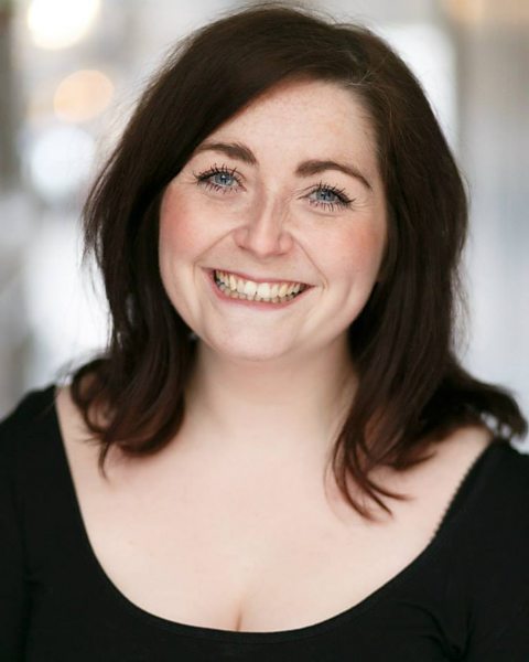 A photograph of Katie Brennan, a teacher and Live Lessons presenter, wearing a black top and smiling.