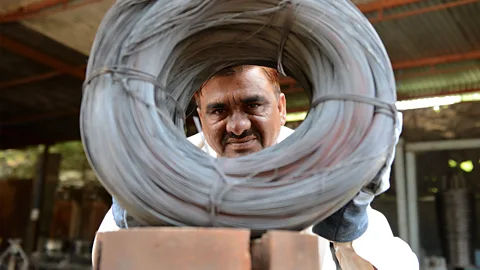 SAM PANTHAKY/AFP via Getty Images Niyazahmed Shaikh peers through coiled wires made from scrap steel strips in his factory in India (Credit: Sam Panthaky/Getty Images)