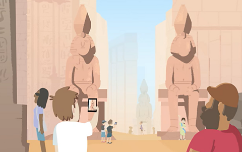 Tourists take photos on their phones of an Ancient Egyptian building. 