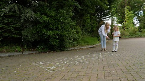 A mum and her daughter stand at the beginning of a hopscotch game.