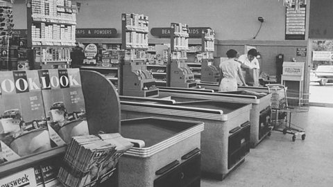 A photograph of a very quiet food store with one cashier and one customer